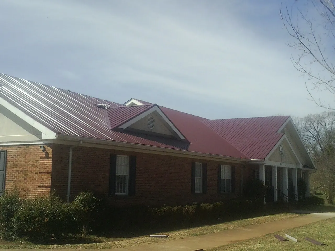Red metal roof with gabled entries on a long brick building, from a Hail Damage Roof Repair job in Lindsay